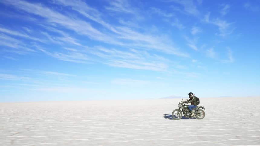 Motorcyclist with a helmet a black leather jacket and jeans rides a motorcycle across the large white sand desert