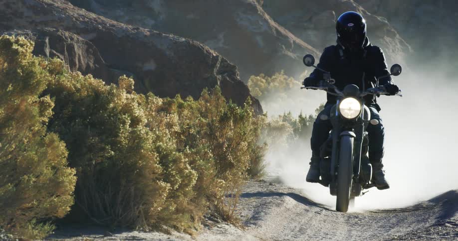 Man with a helmet a leather jacket and jeans rides a motorcycle on dirt road