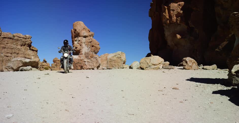 A person rides their motorcycle past the rocks