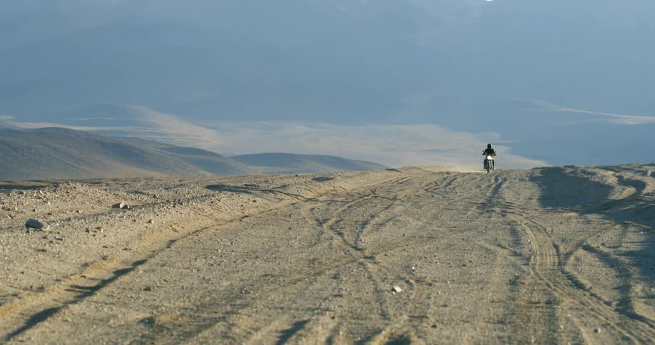 A motorcyclist rides off road through the desert during the day