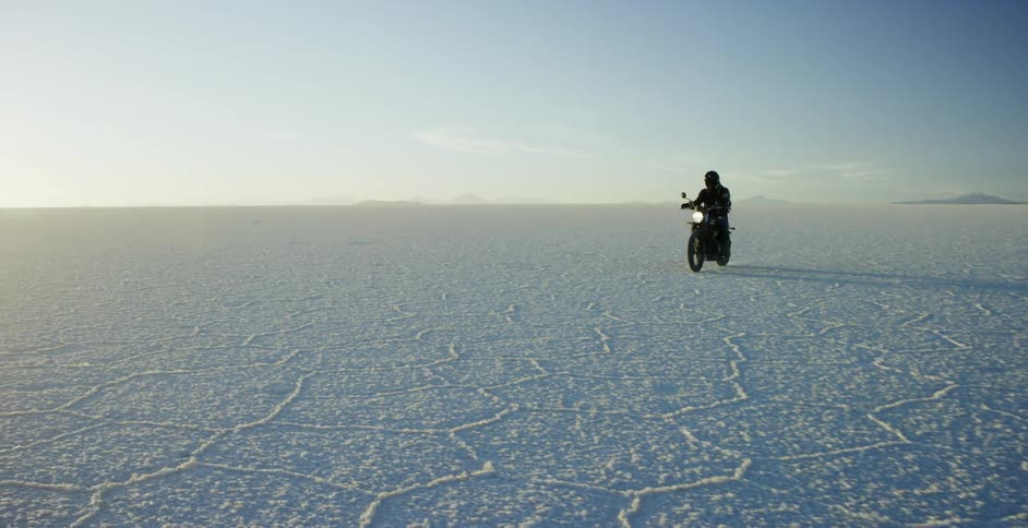 A person rides a motorcycle across a flat and frozen arctic landscape
