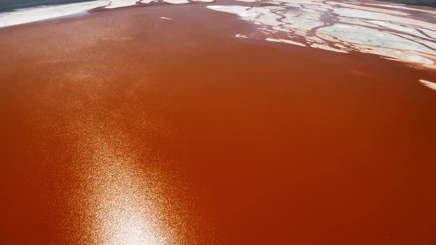 A body of reddish water in a barren plain below a low mountain range