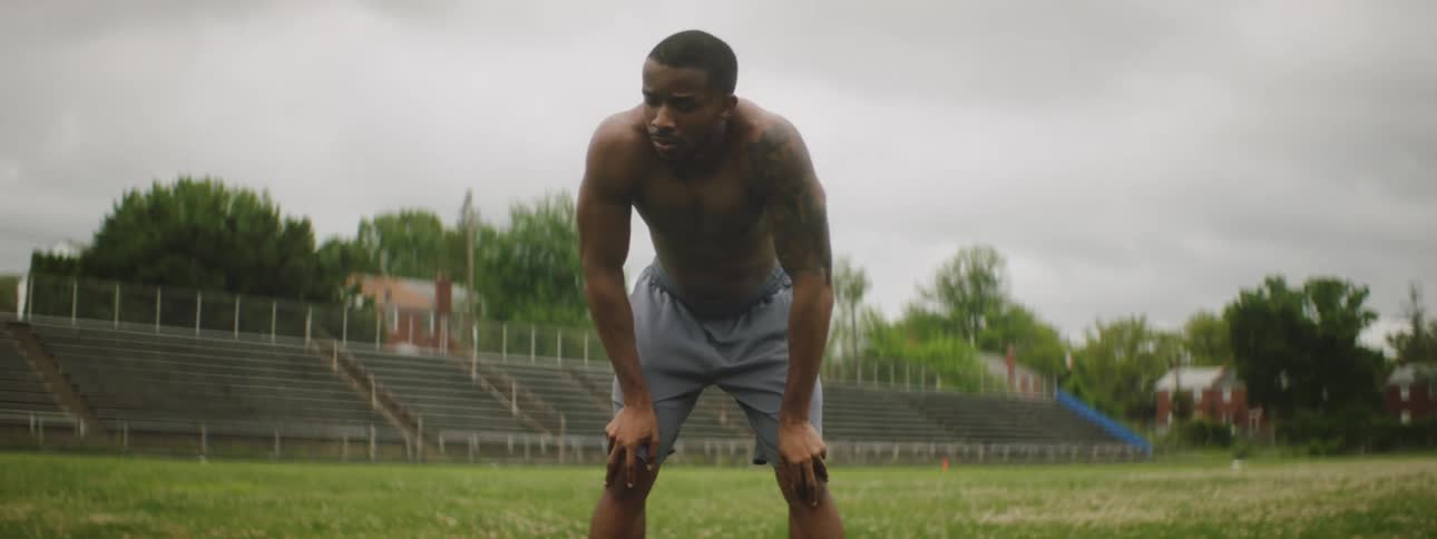 A young black man bends over and catches his breath at a stadium