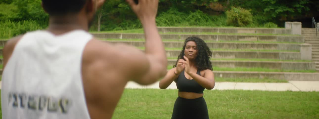 A man and a woman exercising with an exercise ball with trees in the background