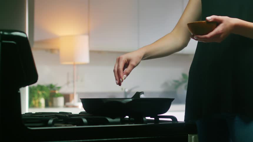 Womans hand adds a pinch of spice to food in a pan on the stove