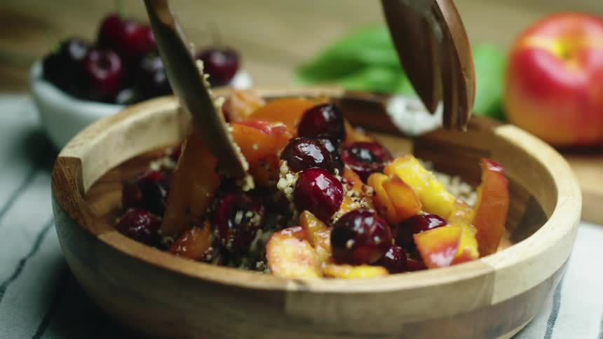Two wooden spoons mixing fruit and seeds in a bowl on a table