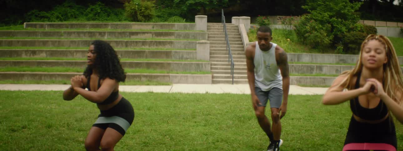 Two women and one man exercising with stairs and trees in the background