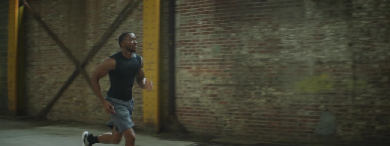 A man runs sprints in an alley beside a factory