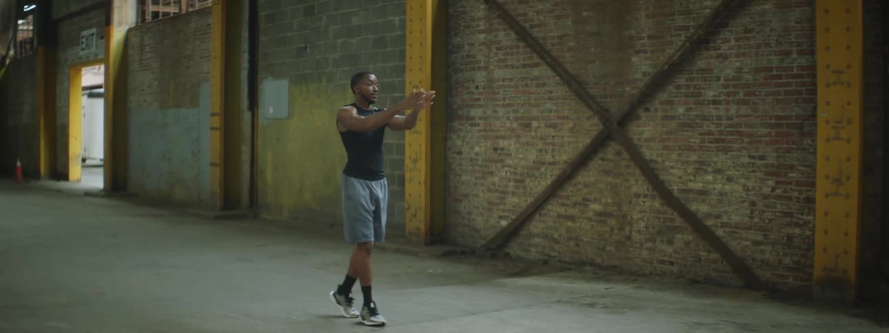 A man moves backwards in a large empty warehouse in fitness gear