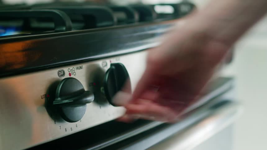 A person turning a dial on the stove and turning up a blue flame