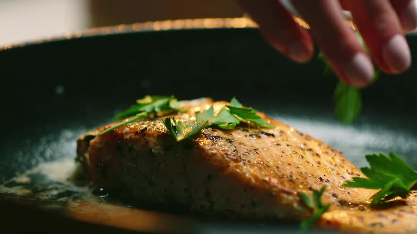 A person putting herbs on fish in a pan