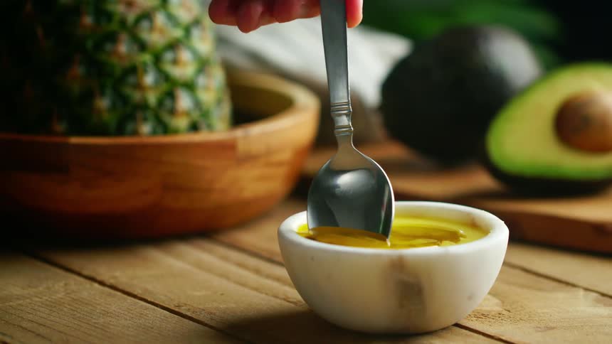 Person stirs mixture in small bowl near sliced avocado and pineapple