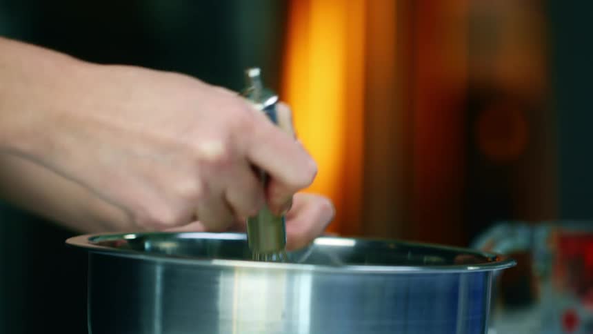 A person uses a metal whisk to stir the contents of a saucepan