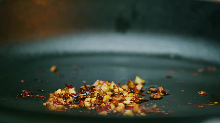 A woman adds spices in to a pan and stirs them