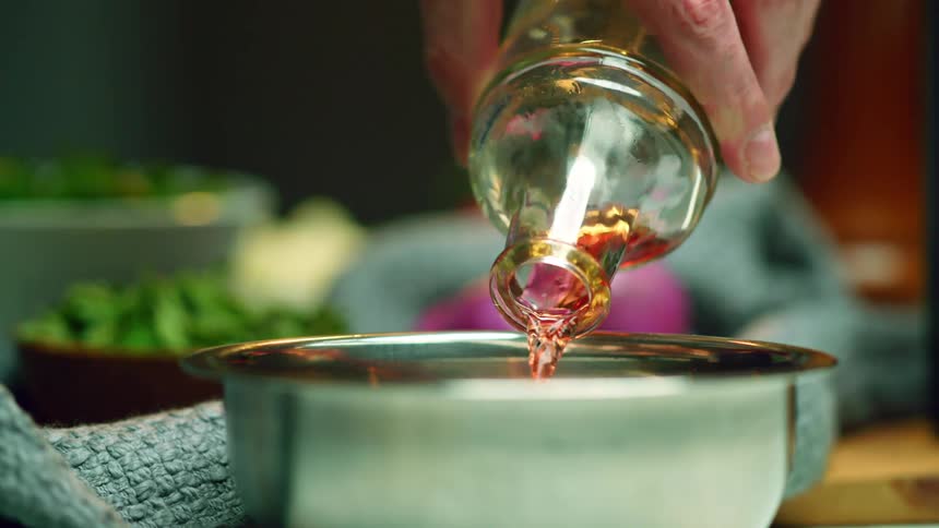 A person pours a bottle of liquid into a metal bowl while cooking