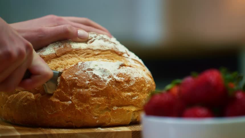 Womans hands cut a slice of sourdough bread on the cutting board in the kitchen
