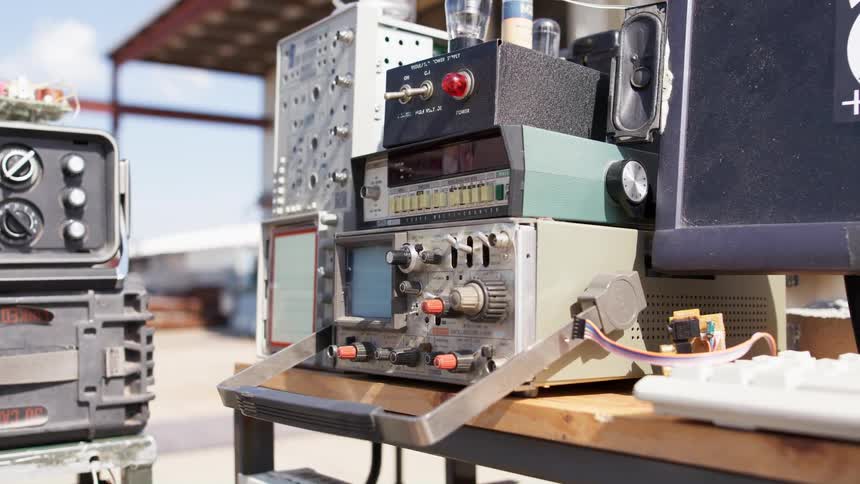 A computer sits next to dispatch equipment and radios on an outdoor desk near a vehicle bay