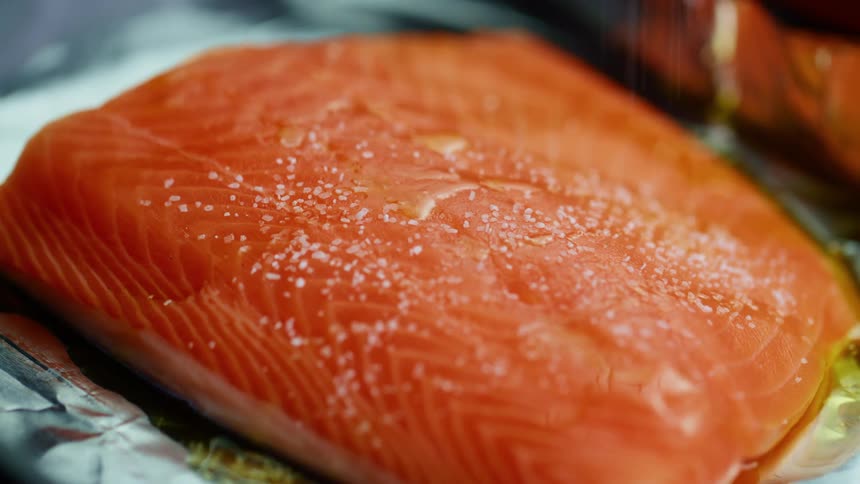 Salt being sprinkled on salmon on a plate