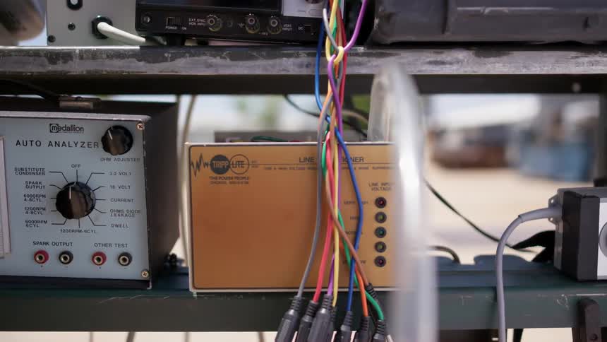 A member of a racing pit crew connects tubes and wires on a device to measure vehicle voltage