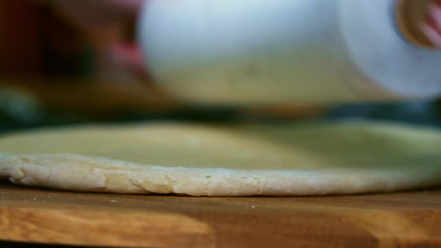 A person flattening dough with a rolling pin on a cutting board