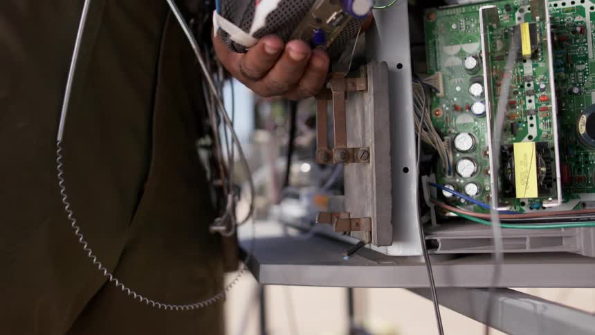 A man lifts up a latch that attached a computer tower to a desk outdoors