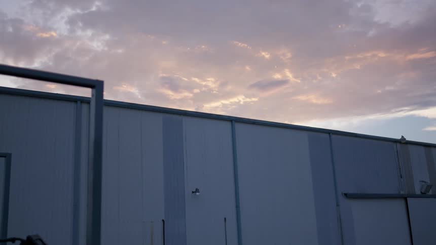 Clouds over warehouse building are tinted pink