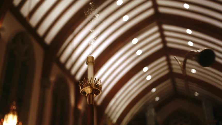 A woman uses a candle snuffer shaped like a bell to put out a tall candle in a church