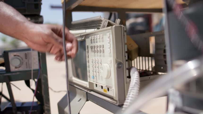 Man adjusts settings on machine sitting on shelf with other machines outside