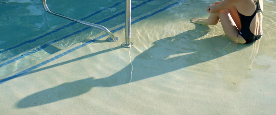 Long shadow of a woman sitting in the shallow part of a pool at morning