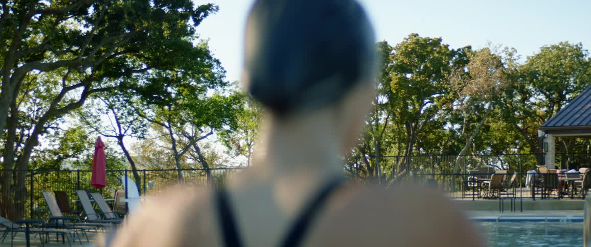 Woman in swimsuit and swim cap stands on diving board of outdoor pool