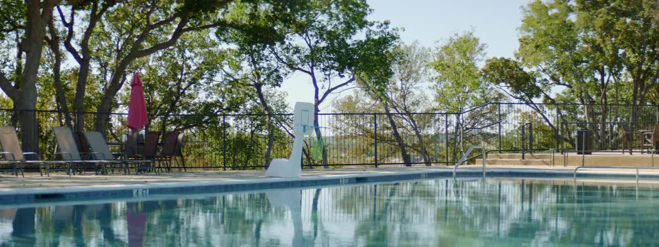 A swimming pool with chairs and railing with trees the sky and clouds in the background