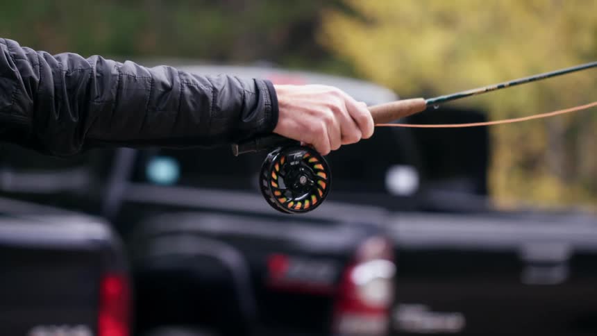 Person wearing black flicks fishing pole near black vehicles