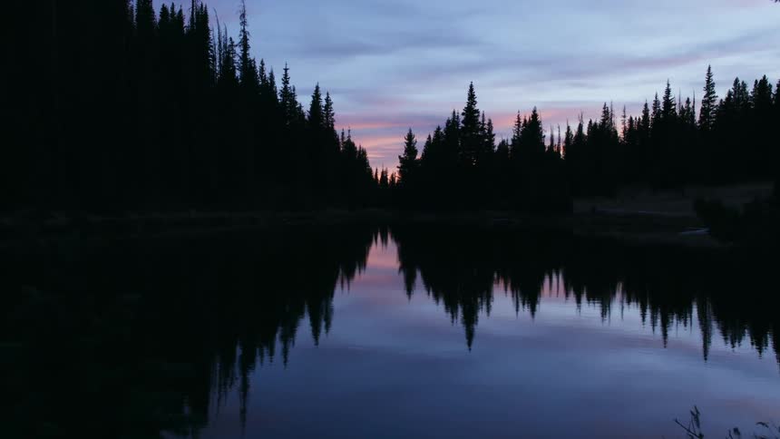 A lake reflects the sky and surrounding forest at sunset