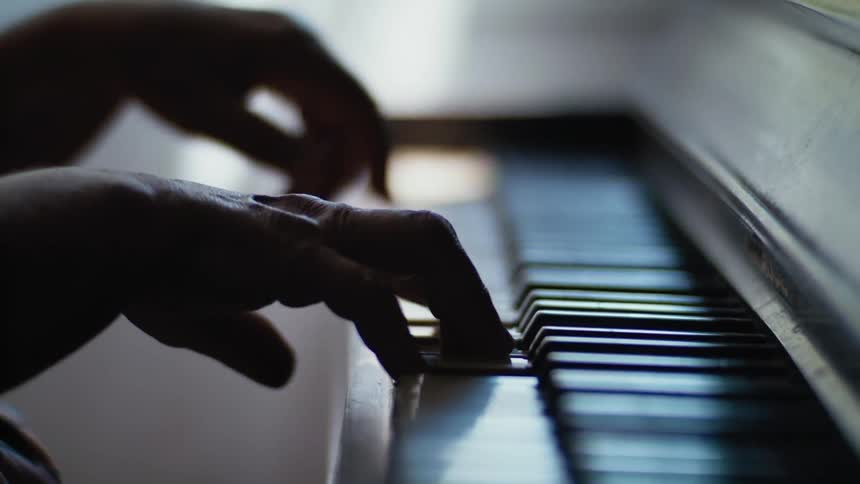 Pianists fingers press on a piano with black and white keys