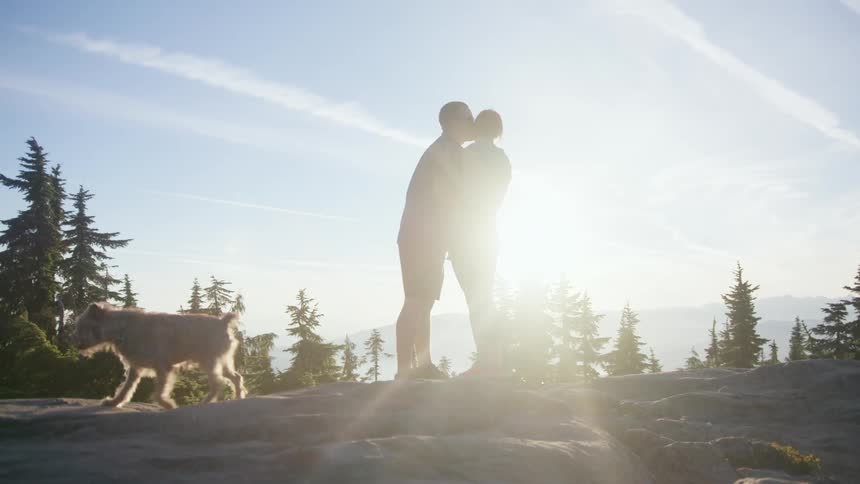 A man and woman stand on a large rock terrain together with their dog
