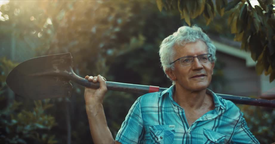 A man rests outside his house with a shovel over his shoulders