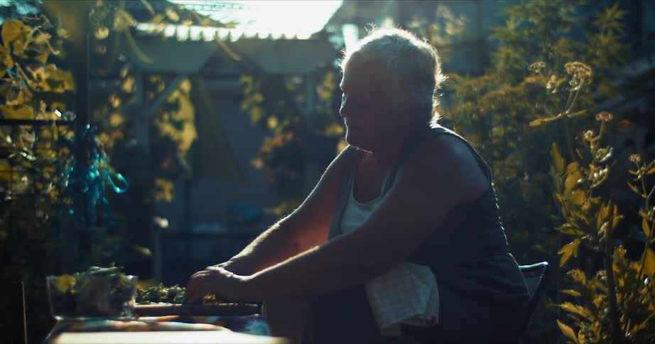 A woman sitting on a chair at a table cutting vegetables on a cutting board