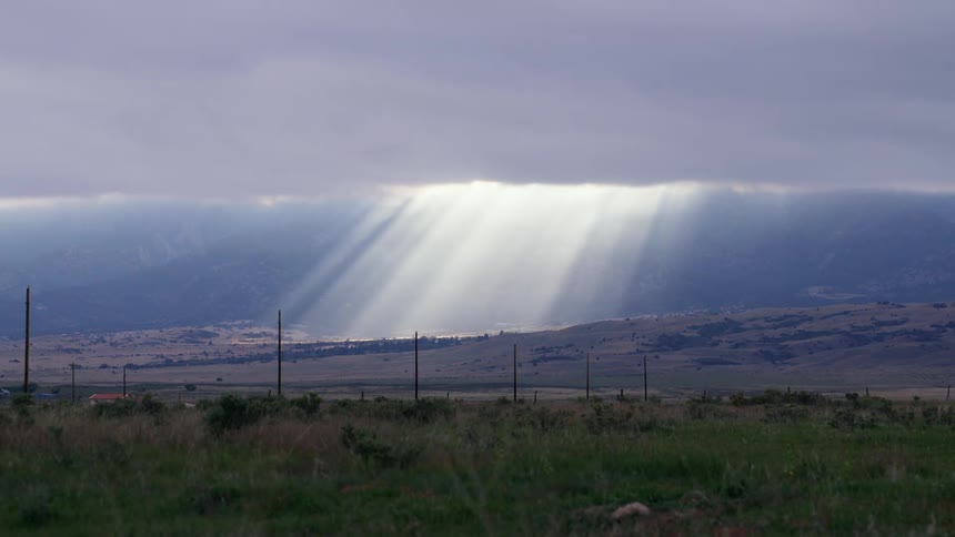 Rays of sunlight shine onto the countryside through a gap in the thick clouds covering the sky