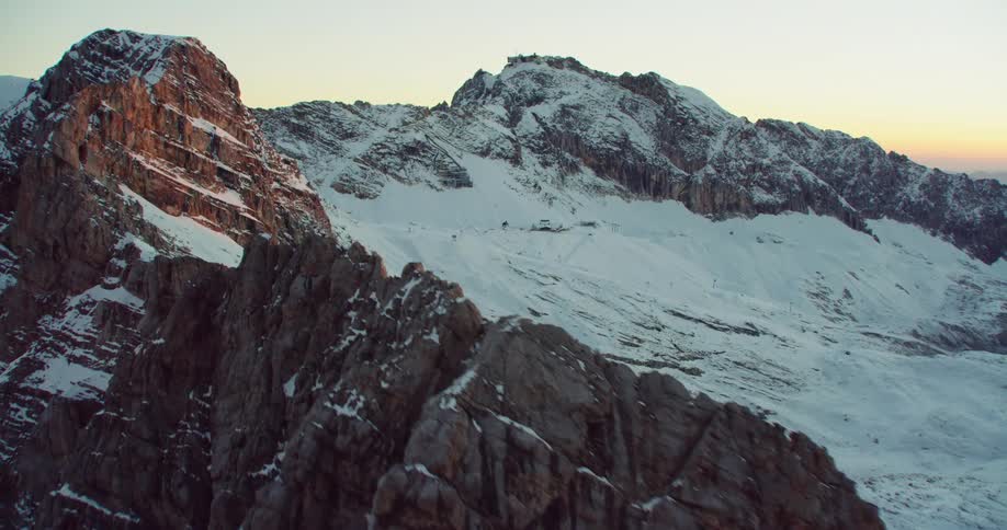 A stone mountain range with one side covered in snow in the evening