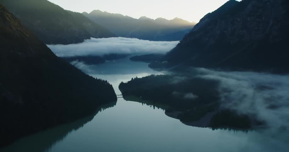 A forest lined river at the bottom of a mountain valley in the evening