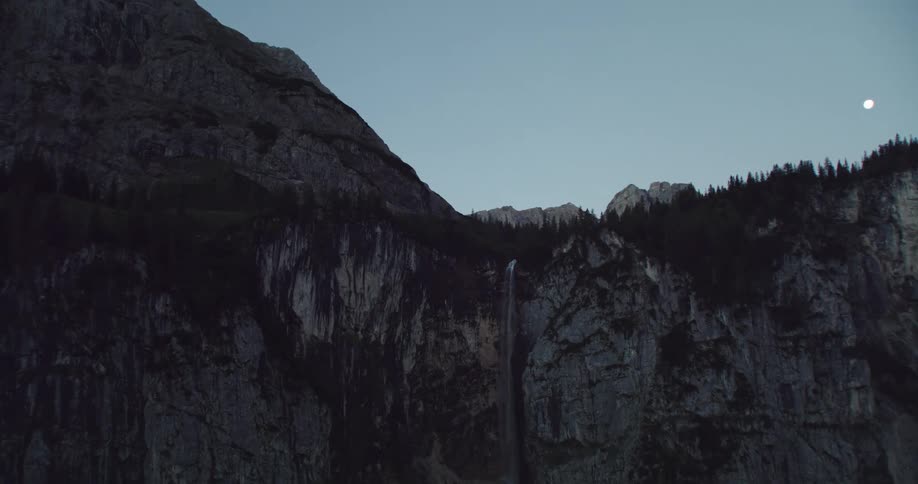 A mountain range with trees and a waterfall with the sky and moon in the background