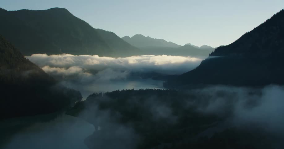 A mountain range near a lake with trees with the sky and clouds in the background