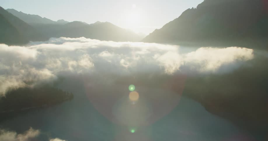 A mountain range near a lake with trees with the sky and clouds in the background