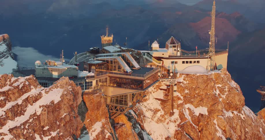 A building on a cliff with a mountain range the sky and clouds in the background