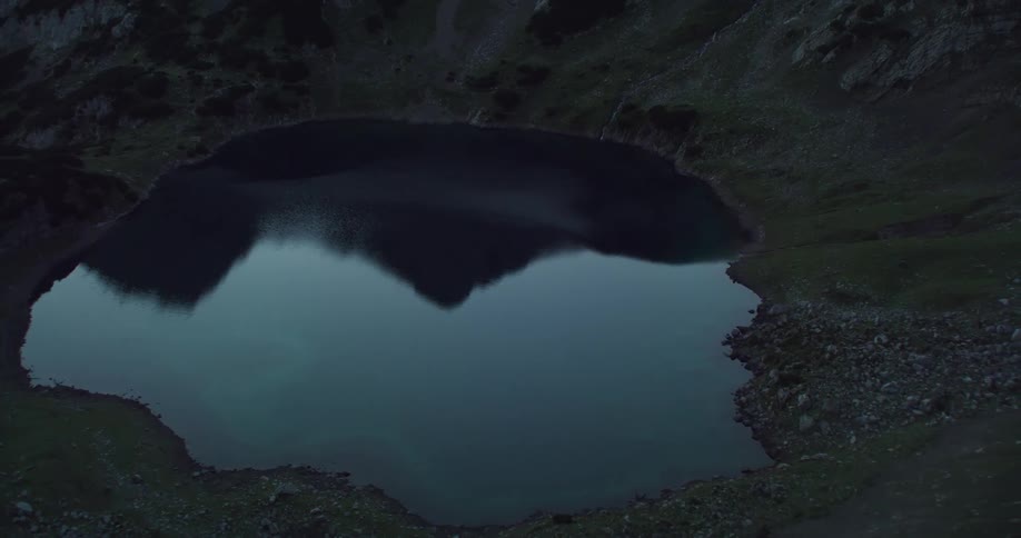 A lake reflecting the mountain ridge surrounding it on a cloudy evening