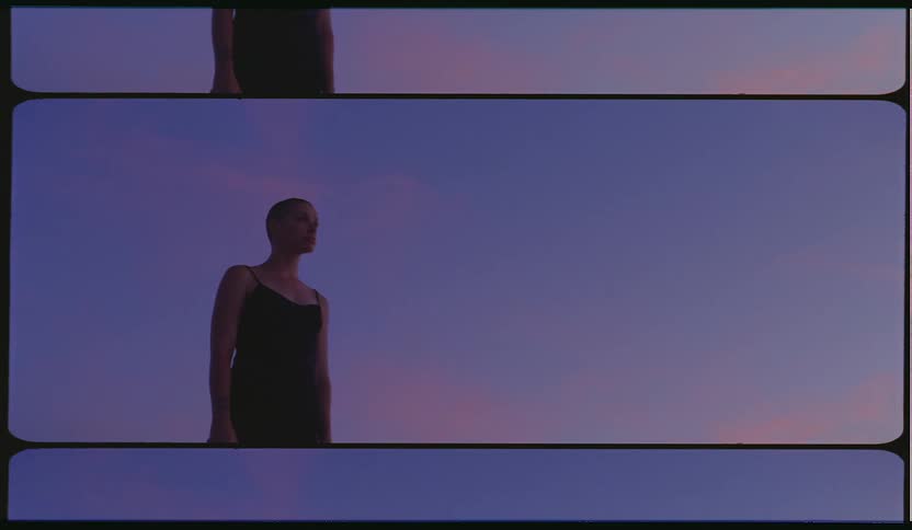 A woman stands motionlessly outside at sunset