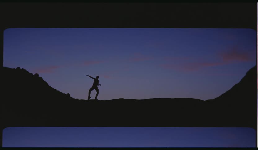 Dancers silhouette moves slowly through dance poses on rough ground