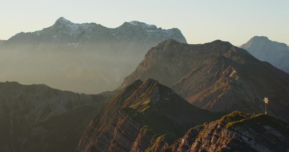 The sun shines upon the sloping sides of multiple huge rocky mountains