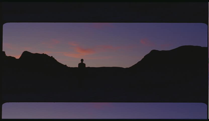 Person silhouetted against mountains walking towards sunset