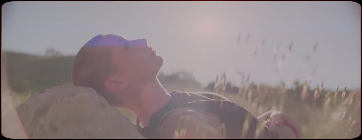 A woman lies in a grassland with her head resting on a stone